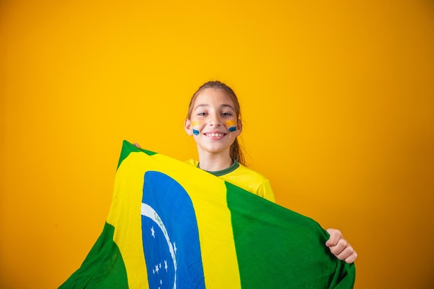 Pequena menina caucasiana com bandeira do Brasil em fundo amarelo. Torcedor infantil brasileiro