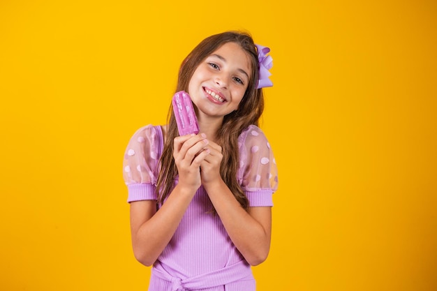 Pequena menina caucasiana com delicioso picolé de uva, sorrindo, olhando para a câmera. Verão