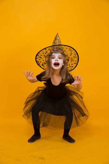 Foto pequena menina em traje de bruxa de halloween, superfície laranja.