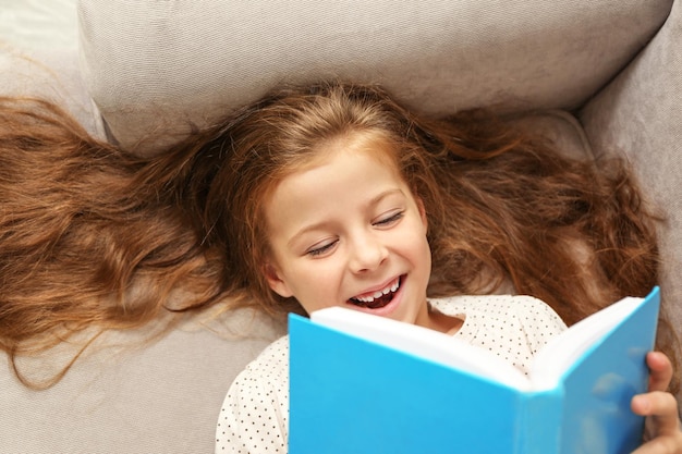 Pequena menina lendo livro no sofá