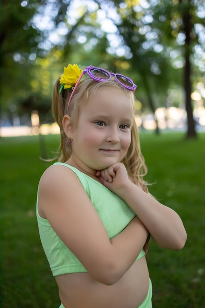 Pequeña modelo posando en el parque con la mano en la barbilla y niña mirando a la cámara