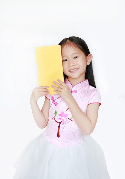 Pequeña muchacha asiática feliz del niño que lleva el vestido cheongsam tradicional rosado que sonríe mientras que recibe el paquete del sobre del oro del Año Nuevo chino aislado. Feliz año nuevo chino concepto.