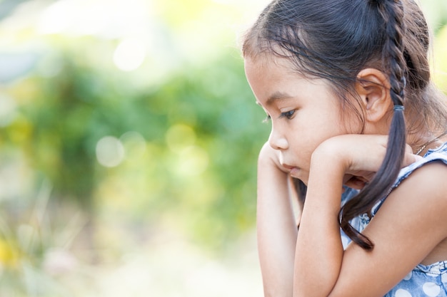 La pequeña muchacha asiática linda del niño descansa su barbilla en sus manos con la sensación aburrida en exterior en tono del color del vintage