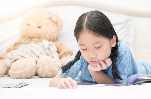 pequeña muchacha asiática linda que lee el libro de cuentos de hadas en la cama, concepto de la educación