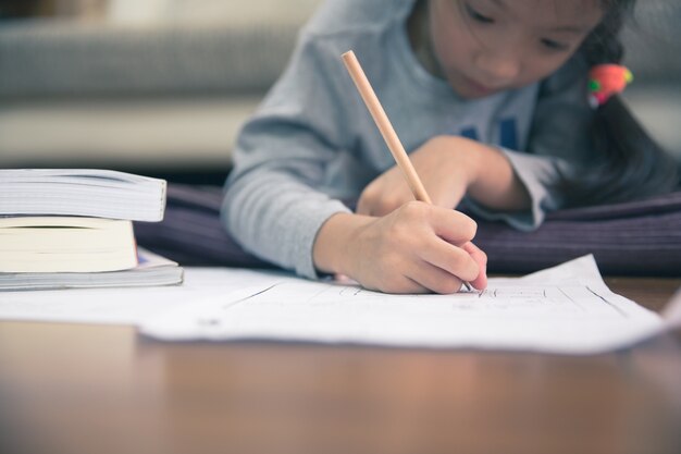 Pequeña muchacha asiática que escribe el papel y que miente en piso