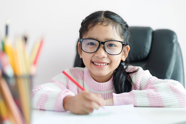 La pequeña muchacha asiática que hace la preparación y la sonrisa con la felicidad para el concepto de la educación seleccionan la profundidad del foco baja del foco