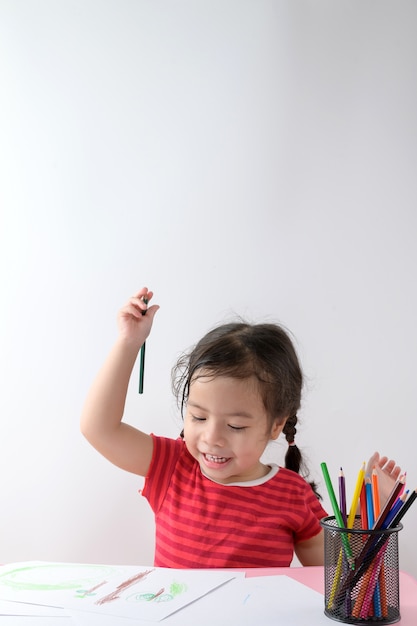 La pequeña muchacha asiática rizada disfruta dibujando en casa. Concepto de educación