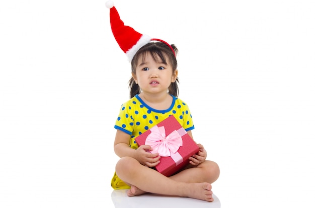 Pequeña muchacha asiática en el sombrero de Papá Noel y la caja de regalo de la Navidad aislados en blanco