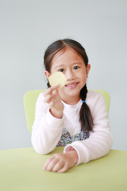 Pequeña muchacha asiática sonriente del niño que come las patatas fritas crujientes en blanco.