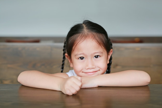 Pequeña muchacha asiática sonriente del niño que miente en la tabla de madera con la mirada de la cámara.