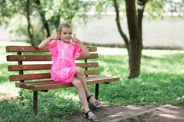 Pequeña muchacha caucásica que se sienta en parque en banco.