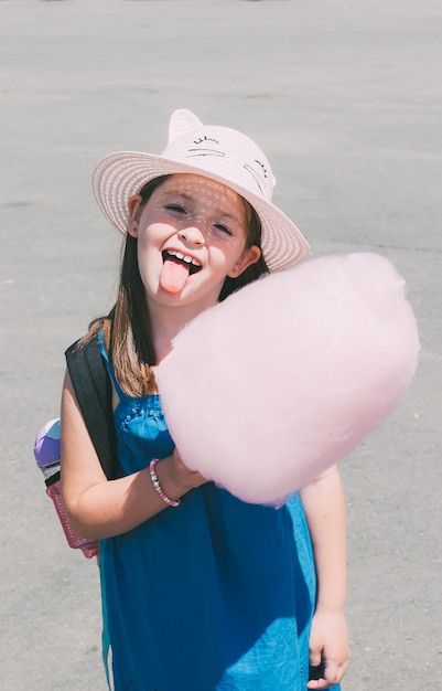 La pequeña muchacha divertida preescolar adorable muestra la lengua con seda rosada del caramelo.