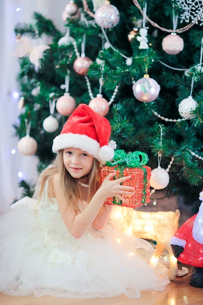 Pequeña muchacha linda cerca del árbol de navidad. Niños bajo el árbol de navidad con cajas de regalo.