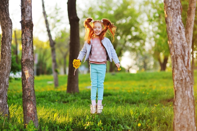 Una pequeña muchacha pelirroja linda en el fondo de un campo de dientes de león y del verdor.