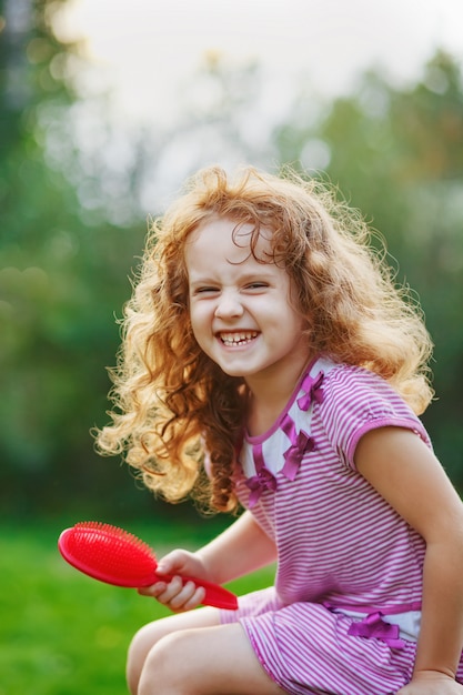 Foto pequeña muchacha rizada sonriente que cepilla su pelo.