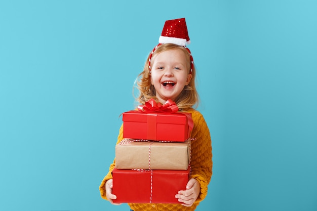 Pequeña muchacha rubia que sostiene tres cajas con los regalos.