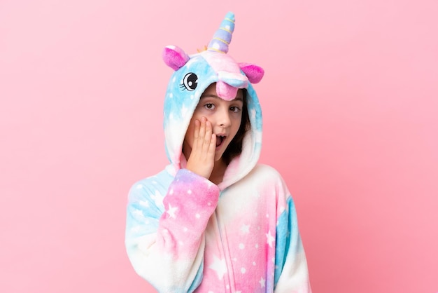 Foto pequeña mujer caucásica con un pijama de unicornio aislado de fondo rosa con expresión facial sorprendida y sorprendida