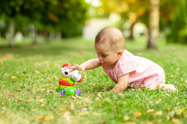 Pequeña niña de 7 meses de edad jugando en un césped verde con un traje rosa, caminando al aire libre, desarrollo temprano de niños de hasta un año