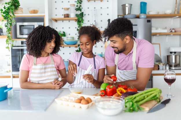 Pequeña niña adorable preparando pastel con padres amorosos y cariñosos en la cocina doméstica familia joven disfruta del proceso de cocina en casa enseñando a los niños a pasar el fin de semana juntos ayudar al concepto de paternidad feliz