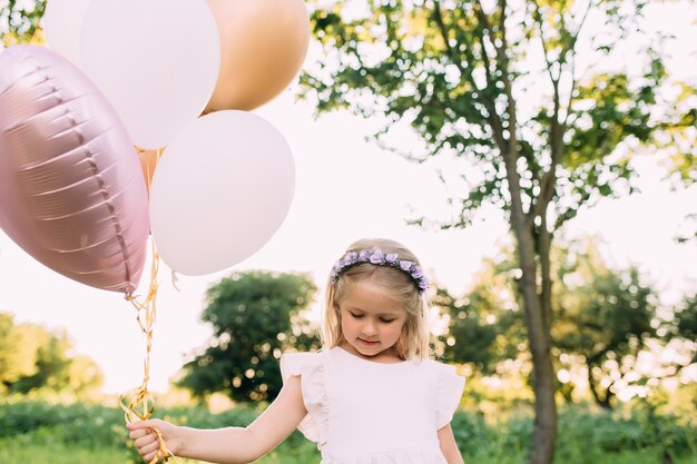 Pequeña niña brillante con globos rosas en el jardín. Foto de alta calidad