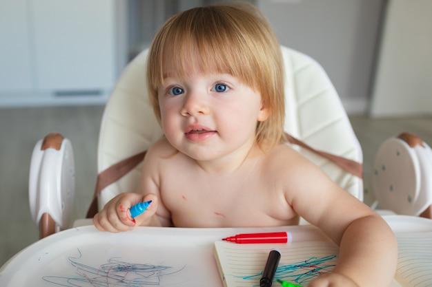 Pequeña niña caucásica dibuja con rotuladores y está toda sucia en pintura