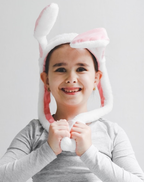 Una pequeña niña caucásica feliz y sonriente en un cuello alto gris con una diadema de conejito