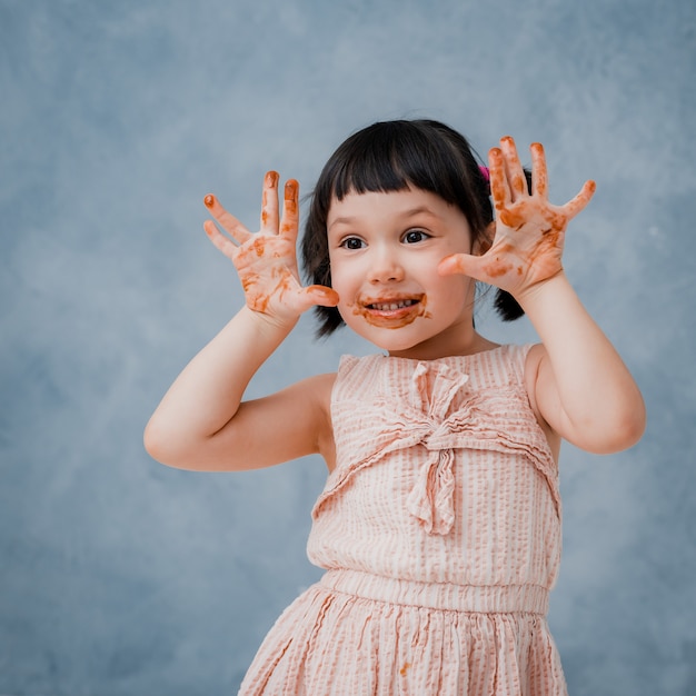 La pequeña niña come chocolate y se lame el dedo en un azul gris