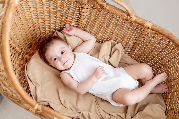 Foto una pequeña niña en una cuna de mimbre en una luminosa habitación infantil con un mono blanco sonríe