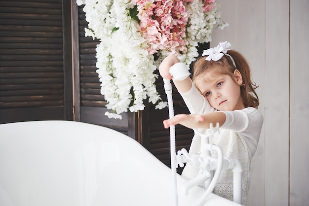 Pequeña niña divertida con el pelo rizado. Prepárate para tomar un baño. Amplio baño iluminado. Un cuerpo sano y limpio. Cuidar de ti mismo desde la infancia