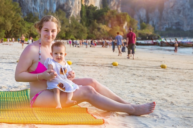 La pequeña niña es traviesa y llora mientras está sentada en las manos de mamá Infante en la playa de arena tropical