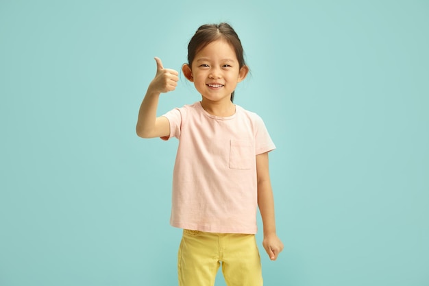 Pequeña niña de etnia asiática levantando el pulgar en aprobación delicioso niño coreano alegremente