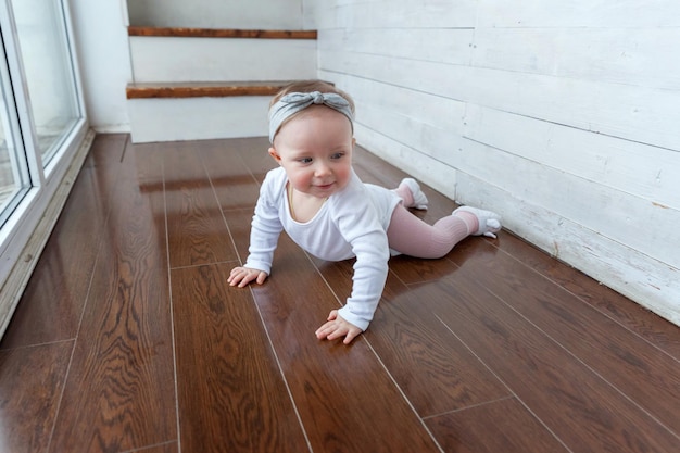 Pequeña niña gateando de un año de edad sentada en el piso con luz brillante en la sala de estar cerca de la ventana smili