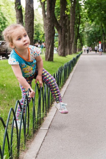 Pequeña niña hermosa sube a través de una valla decorativa en un parque de la ciudad