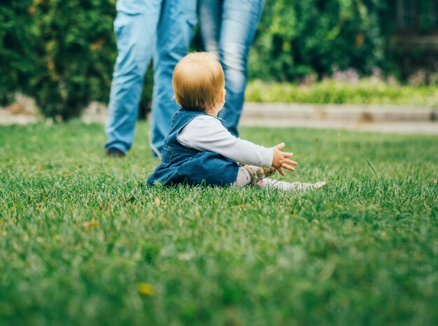 Pequeña niña en jeans vestido sentado en la hierba