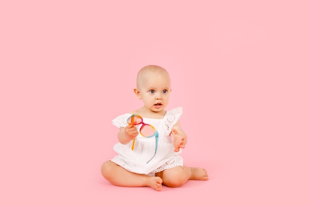 Pequeña niña linda de 1 años con un vestido de verano blanco aislado en rosa pastel