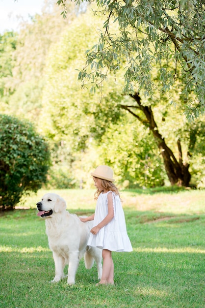 Pequeña niña pequeña linda que juega con su perro de pastor blanco grande. Enfoque selectivo