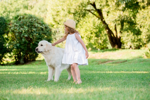 Pequeña niña pequeña linda que juega con su perro de pastor blanco grande.