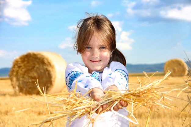 Pequeña niña rural en campo de cosecha con fardos de paja