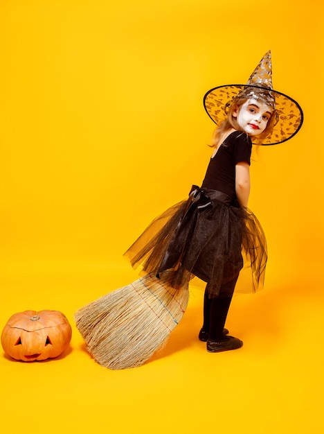 Pequeña niña en traje de bruja de Halloween en novio con calabaza a un lado aislado