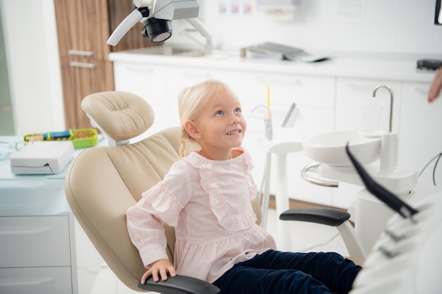 Una pequeña paciente dentista satisfecha mostrando su sonrisa perfecta después del tratamiento dental en una clínica