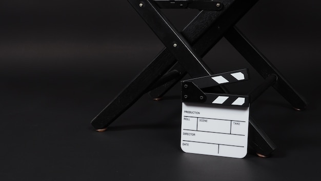 Foto pequeña pizarra blanca para aplaudir o pizarra de cine y silla de director. se utiliza en la producción de video, películas, cine, industria cinematográfica sobre fondo negro.