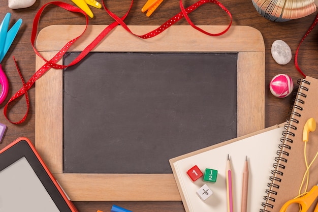 Pequeña pizarra con útiles escolares en la mesa de madera