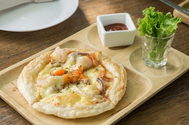 Foto pequeña pizza hawaiana en una placa de madera con la salsa de tomate en restaurante.