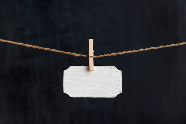 Pequeña placa de identificación Letrero de madera en blanco cuelga con pinzas para la ropa en una cuerda sobre fondo negro. Copie el espacio.