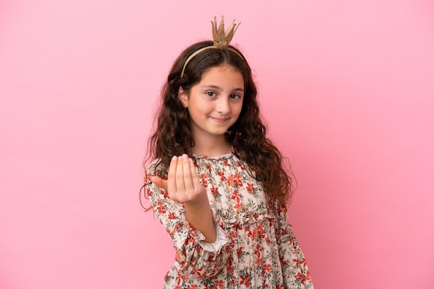 Pequeña princesa caucásica con corona aislada en un fondo rosa invitando a venir con la mano Feliz de que hayas venido