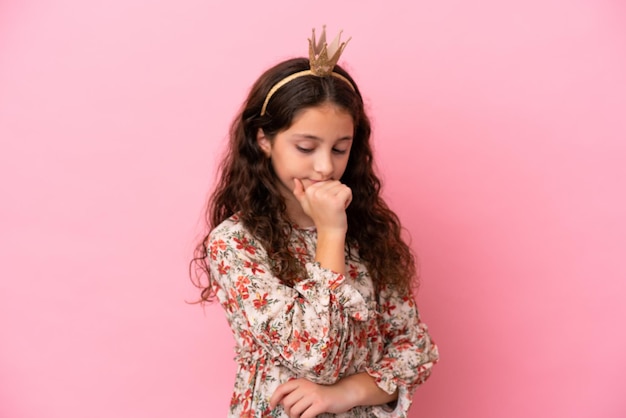 Pequeña princesa caucásica con corona aislada en un fondo rosa mirando hacia un lado y sonriendo