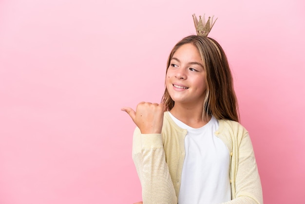 Pequeña princesa con corona aislado sobre fondo rosa apuntando hacia el lado para presentar un producto