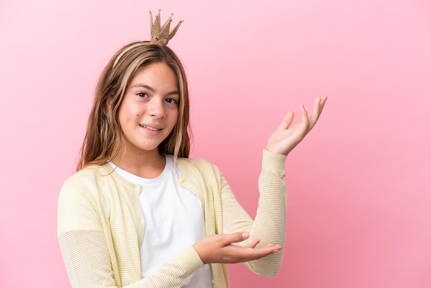 Pequeña princesa con corona aislado sobre fondo rosa extendiendo las manos hacia el lado para invitar a venir