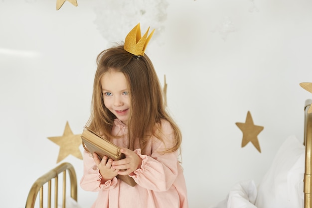 Pequeña princesa con una varita mágica en una cama en una nube sobre un fondo blanco