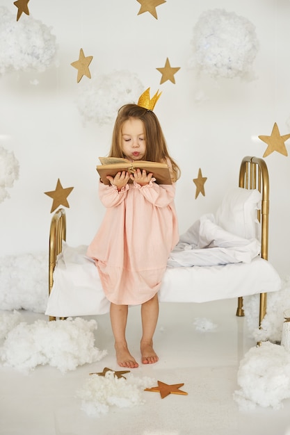 Pequeña princesa con una varita mágica en una cama en una nube sobre un fondo blanco